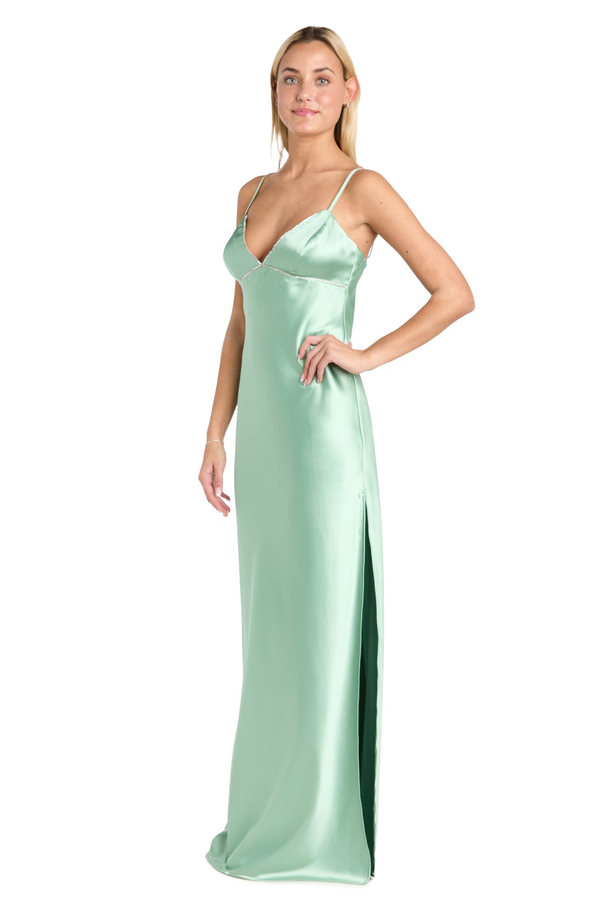 A woman stands wearing the Empire-Waist Long Satin Prom Dress: Morgan 10040N, a light green gown featuring thin straps, a slight v-neckline, and a high side slit—an affordable choice for formal occasions.